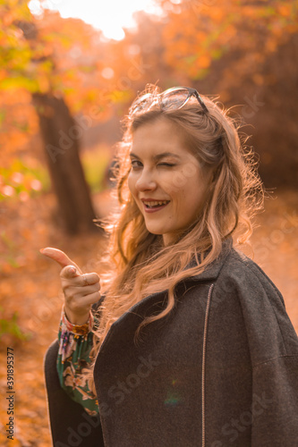 Happy girl in a black cloak stands in chameleon glasses in autumn. Yellow forest  green grass  blonde. wellbeing concept