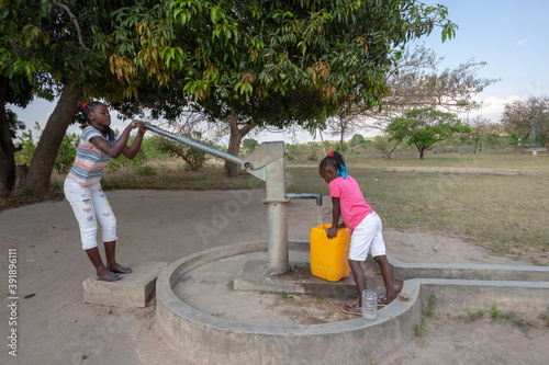 Young girls getting fresh water in the community hand water pump in rural Africa photo