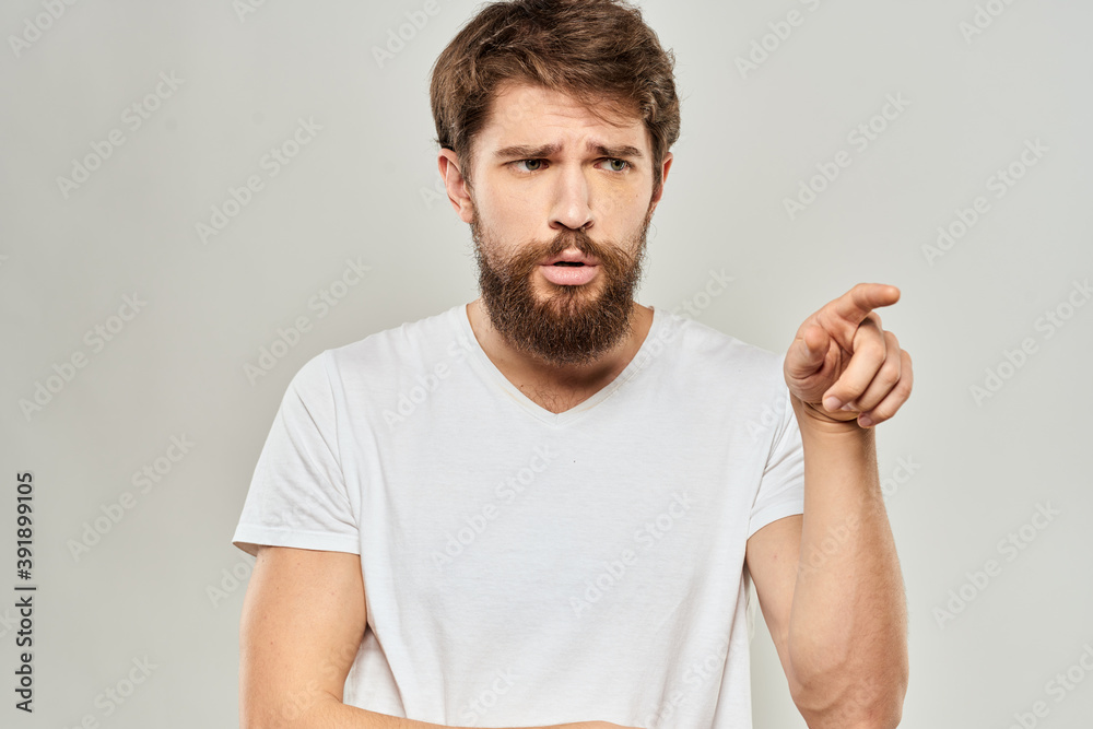 A man in a white t-shirt with a beard emotions displeased facial expression light background A man in a white t-shirt with a beard emotions displeased facial expression light background