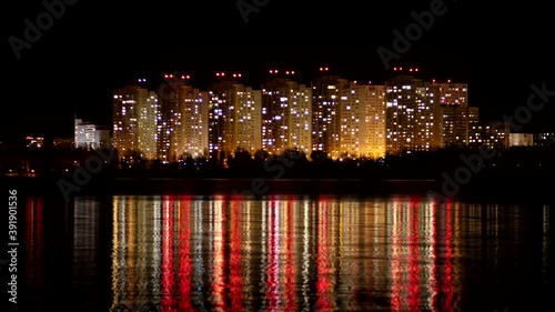 Timelapse. Skyscrapers with signal lights at night reflect light from windows in the river. Buildings on the sea shore. Turns the lights on and off in windows. Night town. Sleeping area on the shore photo