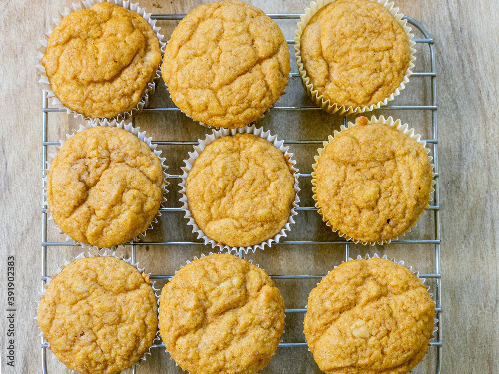 Above view of pumpkin spice muffins arranged on a cooling rack on a brown table. Muffins are a golden color. Above view of pumpkin spice muffins arranged on a cooling rack on a brown table. Muffins are a golden color.