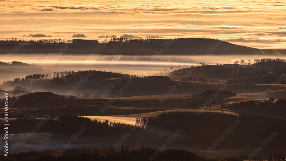 Sun light rays during sunshine peaking through morning mist on a wavy landscape, Jeseniky, Czech Republic.