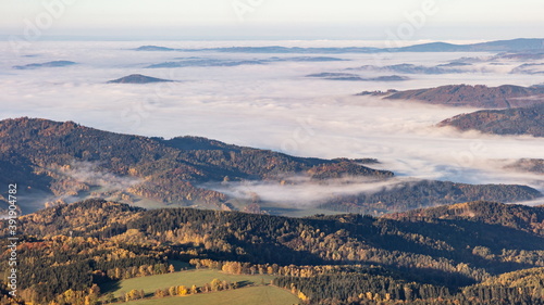 Enlightened autumn hilly landscape from above with morning mist and clouds rolling all over. © Radek Vicar