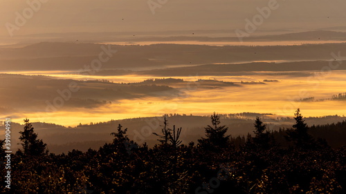Inversion during sunset. Colorful clouds rolling over the hills with dark trees in the foreground.
