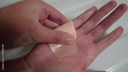 This closeup video shows anonymous hands placing a large band aid on a wounded, injured hand.