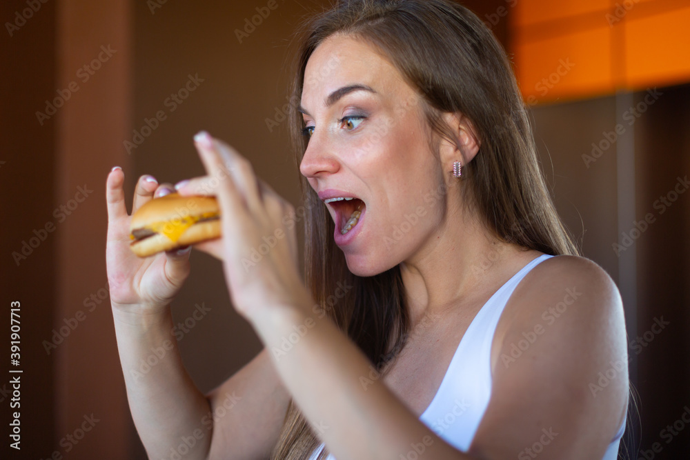 Beautiful hungry young brunette is about to bite a delicious hamburger. Concept of junk food and fast food Beautiful hungry young brunette is about to bite a delicious hamburger. Concept of junk food and fast food