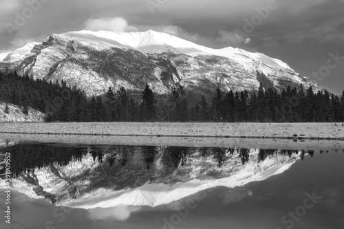 Monochrome Landscape Image of Snowy Mountain Peak reflected in Calm and Cold Lake Water above Canmore, Alberta, Canadian Rockies