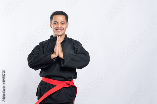 man in pencak silat uniform poses respectfully with both hands cupped in front of his chest on an isolated background