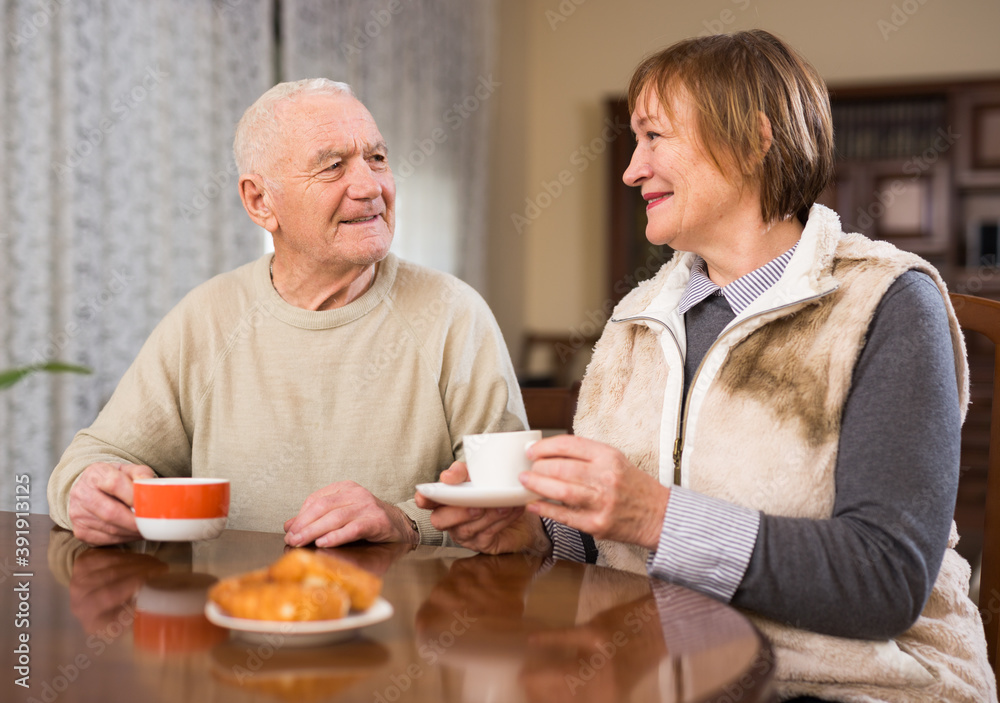 Cheerful elderly man and woman enjoying conversation over cup of coffee at home..