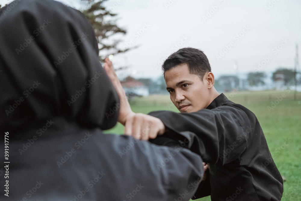 young Asian men wearing pencak silat uniforms with punching movements and women wearing hijabs with a tangkisan movement on outdoor background young Asian men wearing pencak silat uniforms with punching movements and women wearing hijabs with a tangkisan movement on outdoor background