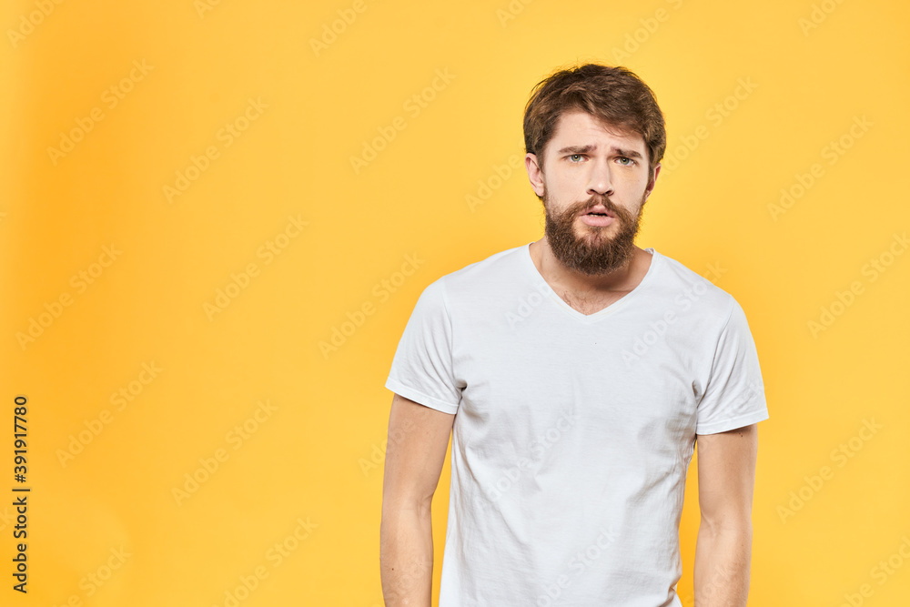 Obraz premium Bearded man in a white T-shirt gestures with his hands emotions studio yellow background