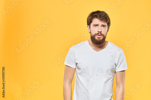 Bearded man in a white T-shirt gestures with his hands emotions studio yellow background