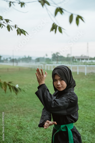 close up of a veiled woman wearing a pencak silat uniform with a side stance movement with a natural background photo