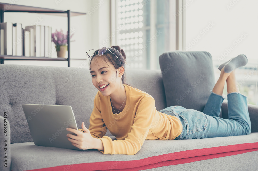 Beautiful young asian woman lying down and using computer laptop talking video conference call on sofa in living room Beautiful young asian woman lying down and using computer laptop talking video conference call on sofa in living room
