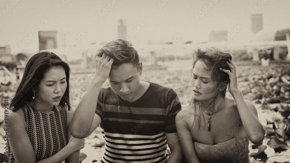Three asian young friends seated on a bench looking at something on the laptop Three asian young friends seated on a bench looking at something on the laptop