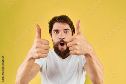 Bearded man emotions fun gesture with hands white t-shirt close-up yellow background