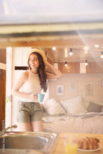 Young woman with cup in trailer, space for text. Camping vacation