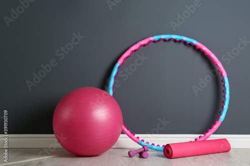 Hula hoop, exercise ball, yoga mat and dumbbells near grey wall in gym photo