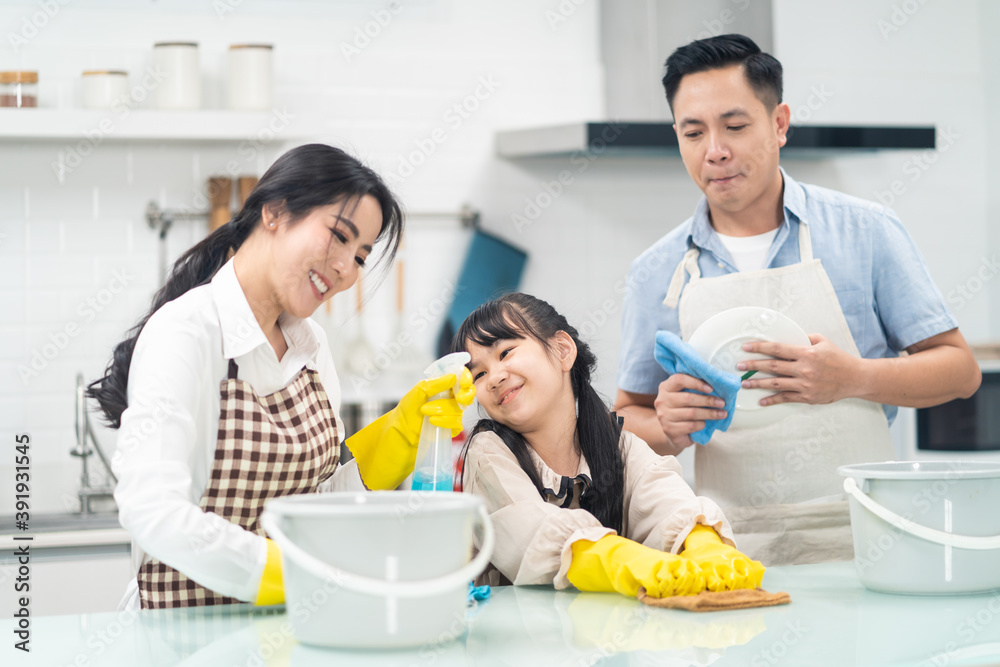 Asian young family teaching their daughter to clean kitchen counter.