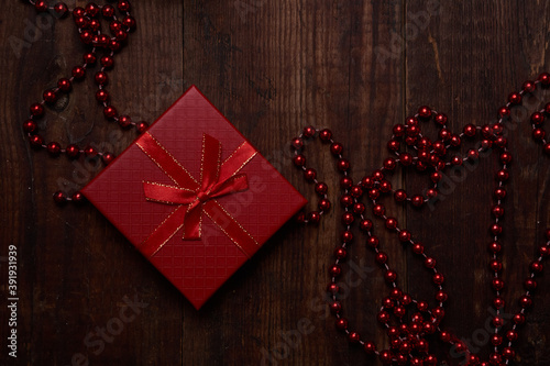 Red Christmas gift with red beads on a brown wooden background with space for text