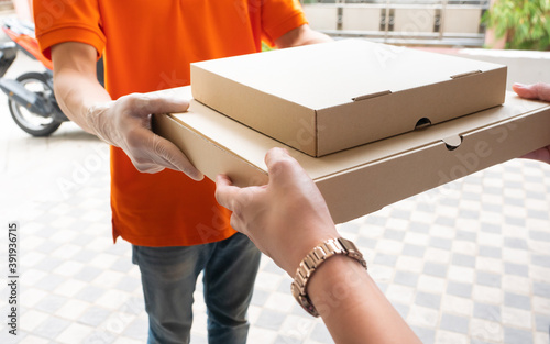 Delivery man who wear orange polo shirt uniform send shipping product from online order in pizza cardboard box to customer that close up holding hand when receive in front of lobby apartment photo
