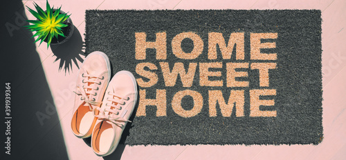Home sweet home doormat. Homeowner moving in new house concept with top view of pink shoes and entrance door mat. Panoramic banner background.