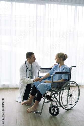 Doctor talking and consultant to patient in wheelchair at hospital.