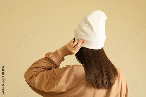 Woman in stylish sweatshirt and beanie on beige background