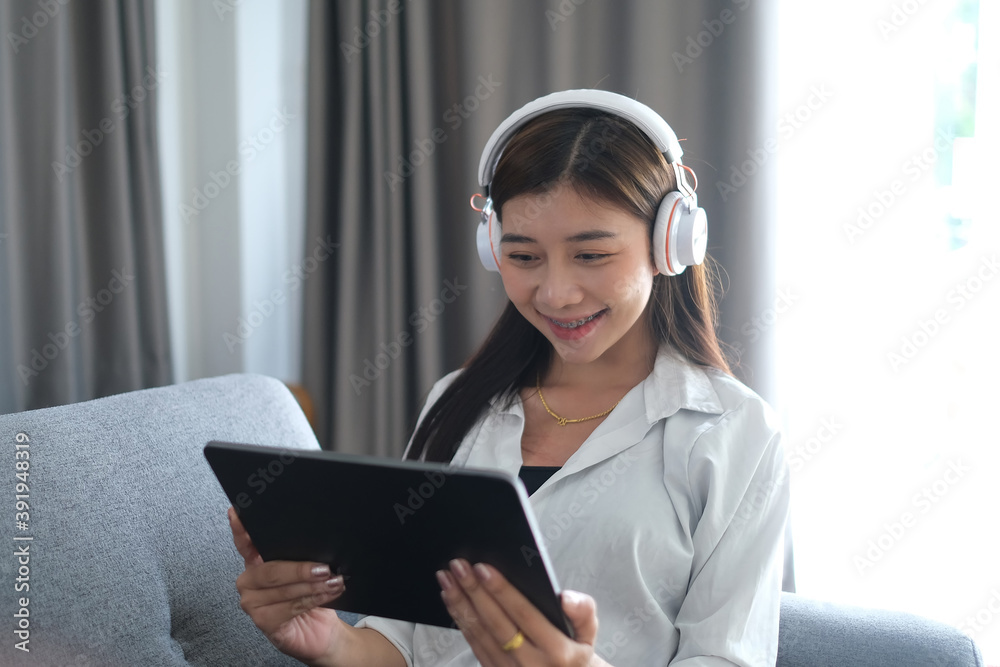 A cheerful woman with headphones sitting on sofa using tablet and enjoying leisure time at home. A cheerful woman with headphones sitting on sofa using tablet and enjoying leisure time at home.
