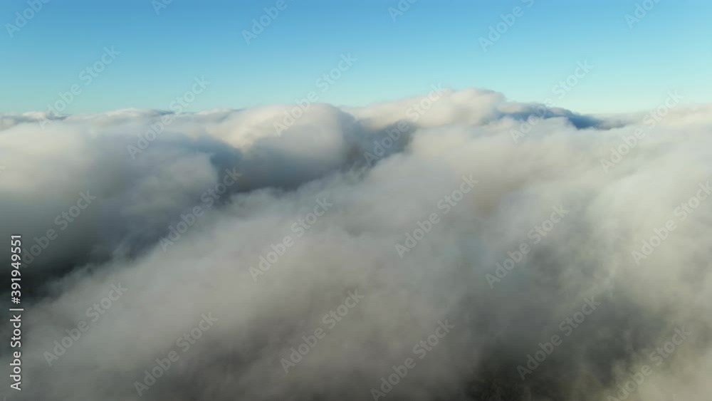 Moving white clouds blue sky on coastline and sea surface scenic aerial view. Drone flies forward high in blue sky through the fluffy clouds on panorama of the sea shore. The sun is hidden. Fog Moving white clouds blue sky on coastline and sea surface scenic aerial view. Drone flies forward high in blue sky through the fluffy clouds on panorama of the sea shore. The sun is hidden. Fog