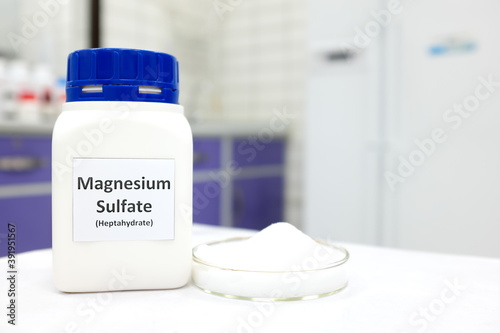 Fotografie Selective focus of magnesium sulfate or epsom salt chemical compound bottle beside a petri dish with white crystalline powder in a chemistry laboratory background