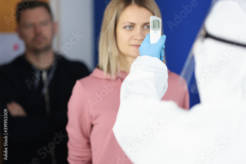 Doctor in protective suit measures the temperature of visitors. Checking the temperature of the population in the coronavirus pandemic concept