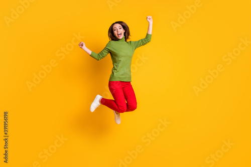 Full body photo of crazy lady jump high up winner raise fists wear pullover sneakers red trousers isolated yellow color background