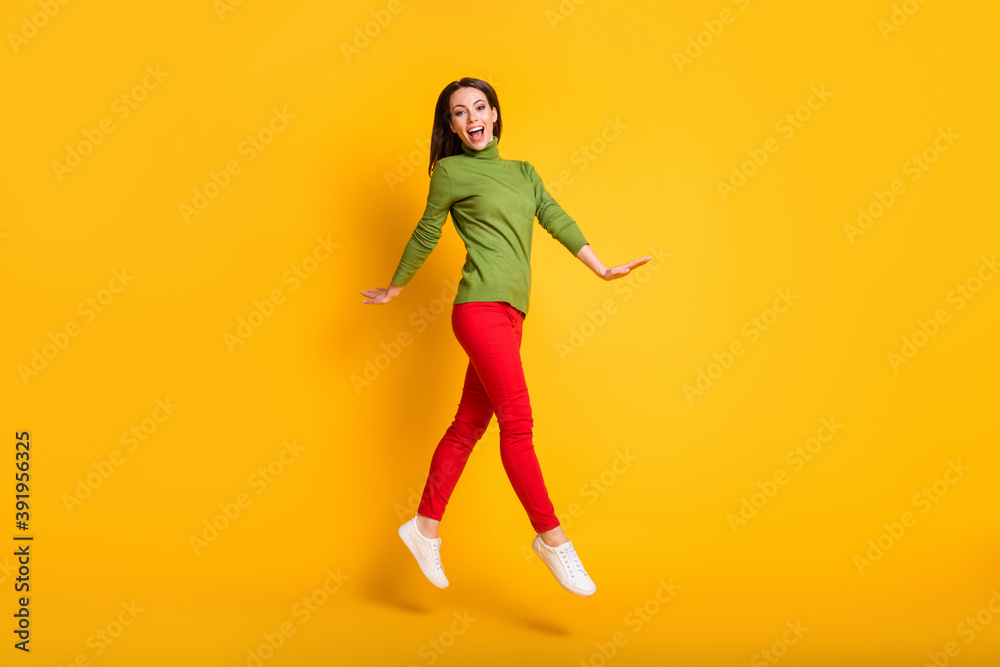 Full size profile photo of funny lady jump up walking wear green pullover sneakers trousers isolated yellow color background Full size profile photo of funny lady jump up walking wear green pullover sneakers trousers isolated yellow color background