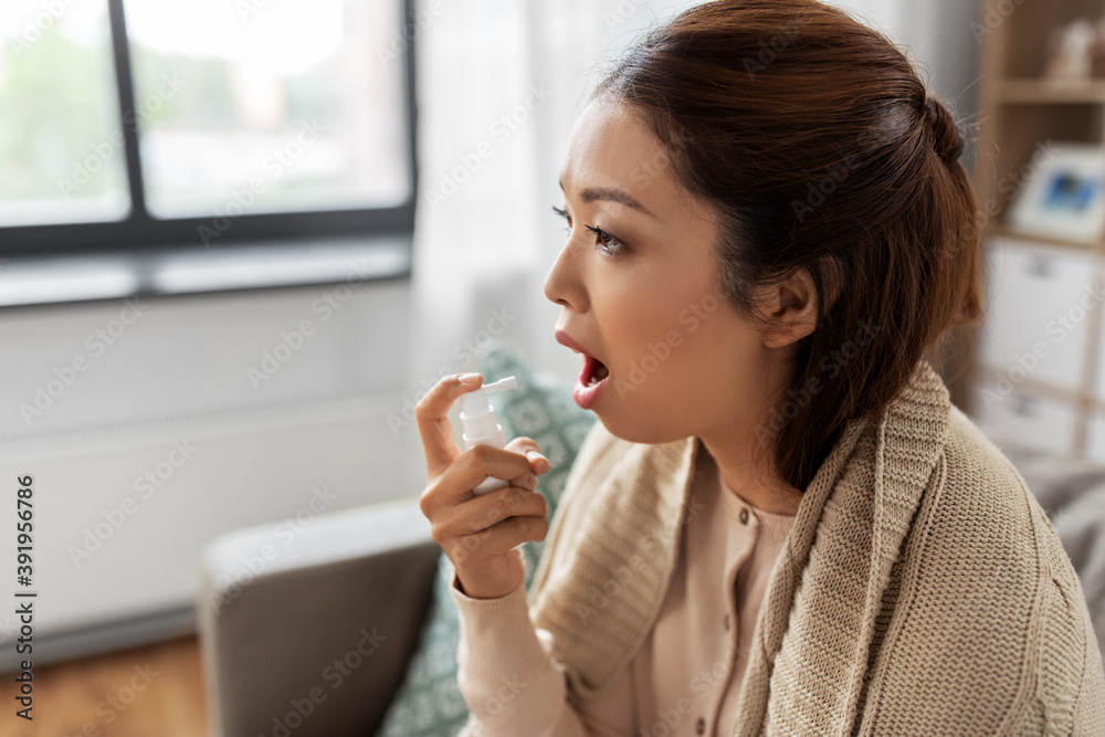 health, cold and people concept - sad sick young asian woman in blanket using oral spray medicine at home health, cold and people concept - sad sick young asian woman in blanket using oral spray medicine at home
