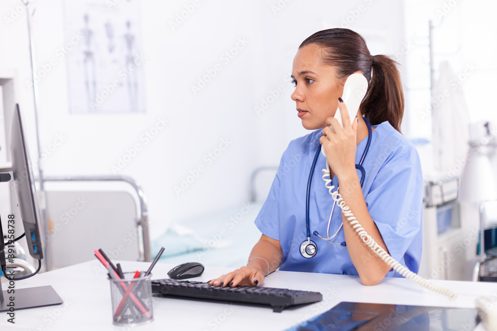 Medical nurse talking with patient on the phone about diagnosis. Health care physician sitting at desk using computer in modern clinic looking at monitor. Medical nurse talking with patient on the phone about diagnosis. Health care physician sitting at desk using computer in modern clinic looking at monitor.