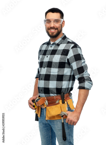 profession, construction and building - happy smiling male worker or builder in goggles with tool belt over white background