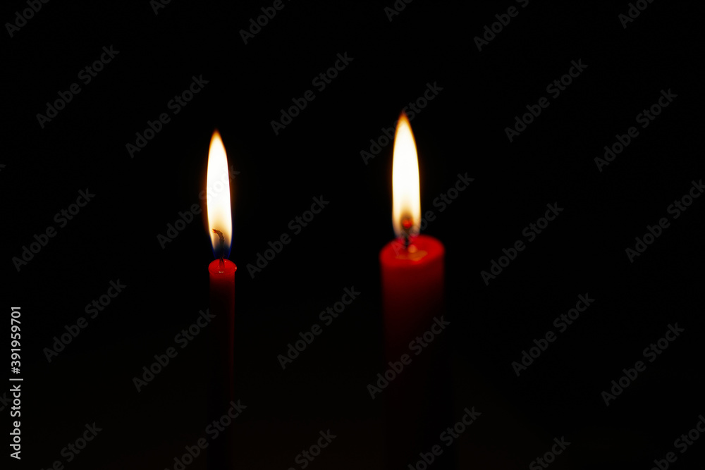 Dark scarlet candles with a burning wick. Burning candles on isolated black background. Candle flame close-up. Dark scarlet candles with a burning wick. Burning candles on isolated black background. Candle flame close-up.