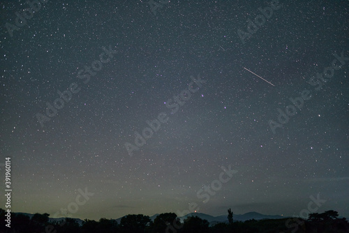 Meteor in the dark night sky. A meteor above the mountains. Starry sky with a passing meteor.