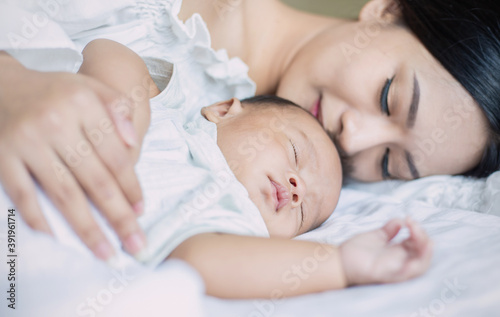 Close up portrait of beautiful young asian or caucasian mother girl kissing her healthy newborn baby sleep in bed with copy space. Healthcare and medical love asia woman lifestyle mother's day concept