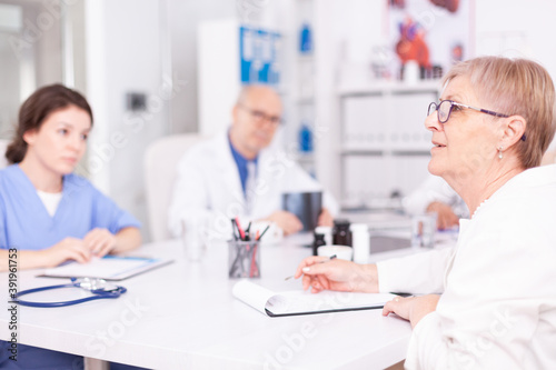 Mature woman doctor explaining diagnosis to medical staff in hospital conference room and having a discussion. Clinic expert therapist talking with colleagues about disease, medicine professional
