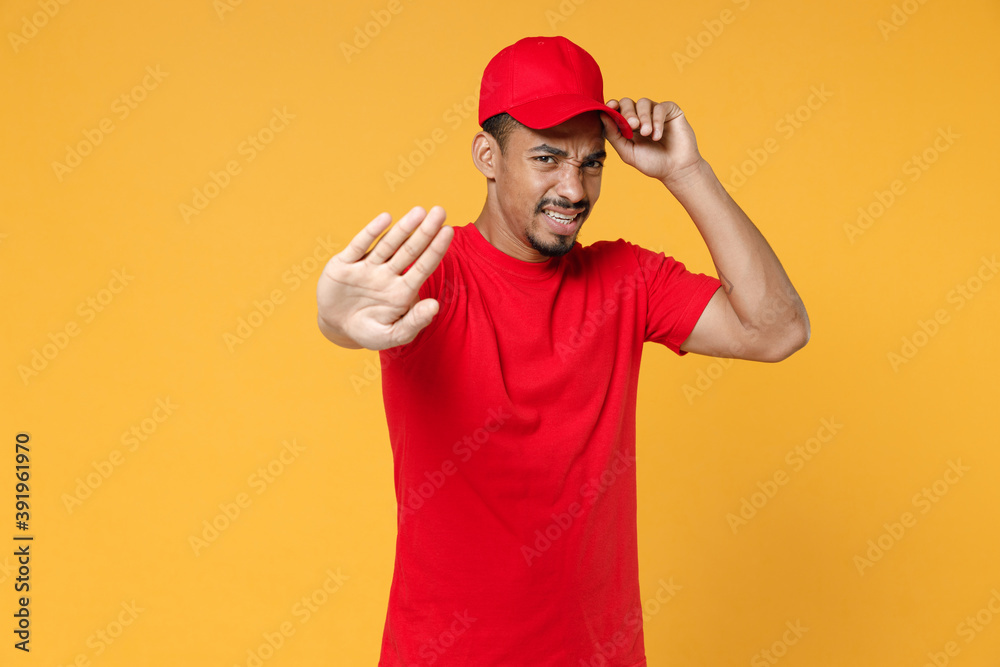 Delivery employee african man 20s in red cap blank print t-shirt uniform workwear work courier dealer service during quarantine coronavirus covid-19 virus concept isolated on yellow background studio. Delivery employee african man 20s in red cap blank print t-shirt uniform workwear work courier dealer service during quarantine coronavirus covid-19 virus concept isolated on yellow background studio.