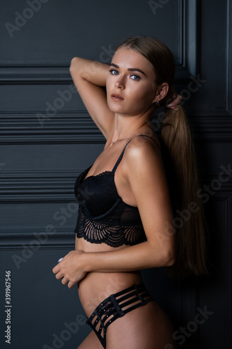 Attractive  beautiful sensual blonde woman wearing black lingerie  playing with hair near classic black wall.