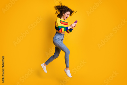 Profile full size photo of cheerful nice curly hair girl jump chat telephone wear pullover jeans sneakers isolated on yellow background