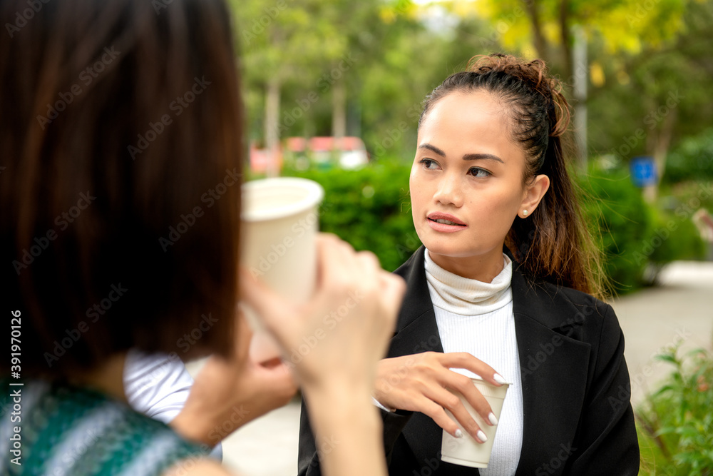 Outdoor business meeting. Asian woman talking to another woman sipping coffee Outdoor business meeting. Asian woman talking to another woman sipping coffee