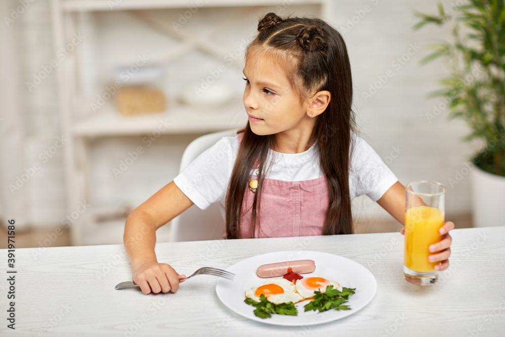 little child girl having breakfast - fried egg and orange juice in the kitchen. healthy breakfast. fried egg face smiles on a white plate little child girl having breakfast - fried egg and orange juice in the kitchen. healthy breakfast. fried egg face smiles on a white plate