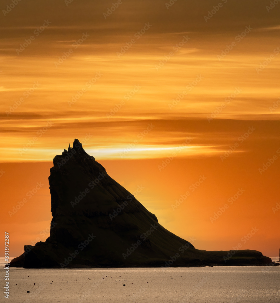 Tindholmur boulder peak against orange sky, backlit