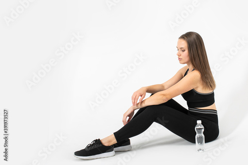 Portrait of fitness woman sitting on the floor in sportswear with bottle of water near of her.