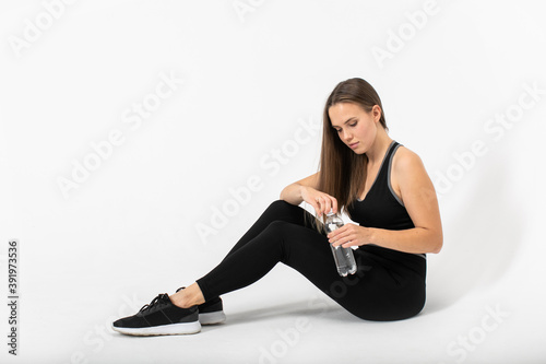 Portrait of fitness woman sitting on the floor in sportswear with bottle of water in her hands.