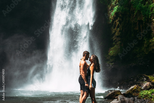Beautiful couple kissing at the waterfall. A couple in love at a beautiful waterfall. Wedding trip to Bali. Honeymoon trip. A man of athletic build kisses a beautiful woman. Vacation in Bali.